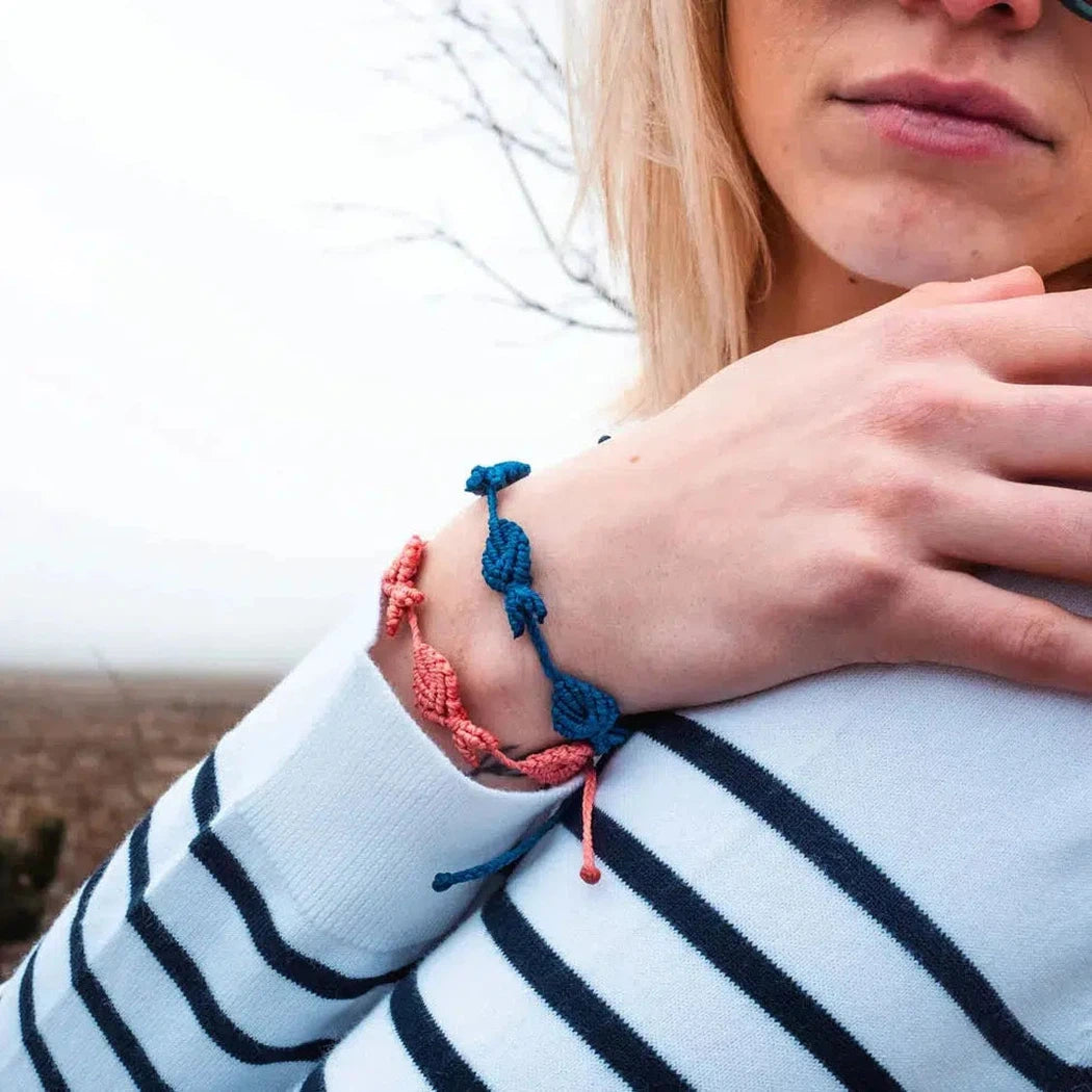 A woman wearing a striped shirt shows off her 4Ocean 4Fish Coral bracelet on her wrist with a foggy outdoor background.