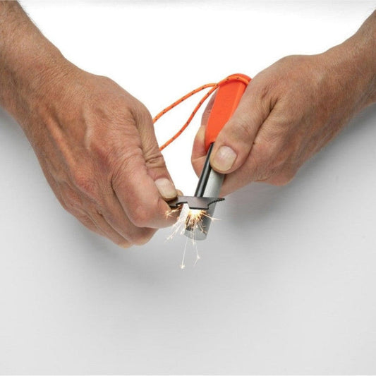 Two hands hold the Adventure Medical Kits Mag Striker with Tinder Cord, which is sparking as one hand scrapes the striker against the metal base, with an orange cord attached and a white background.