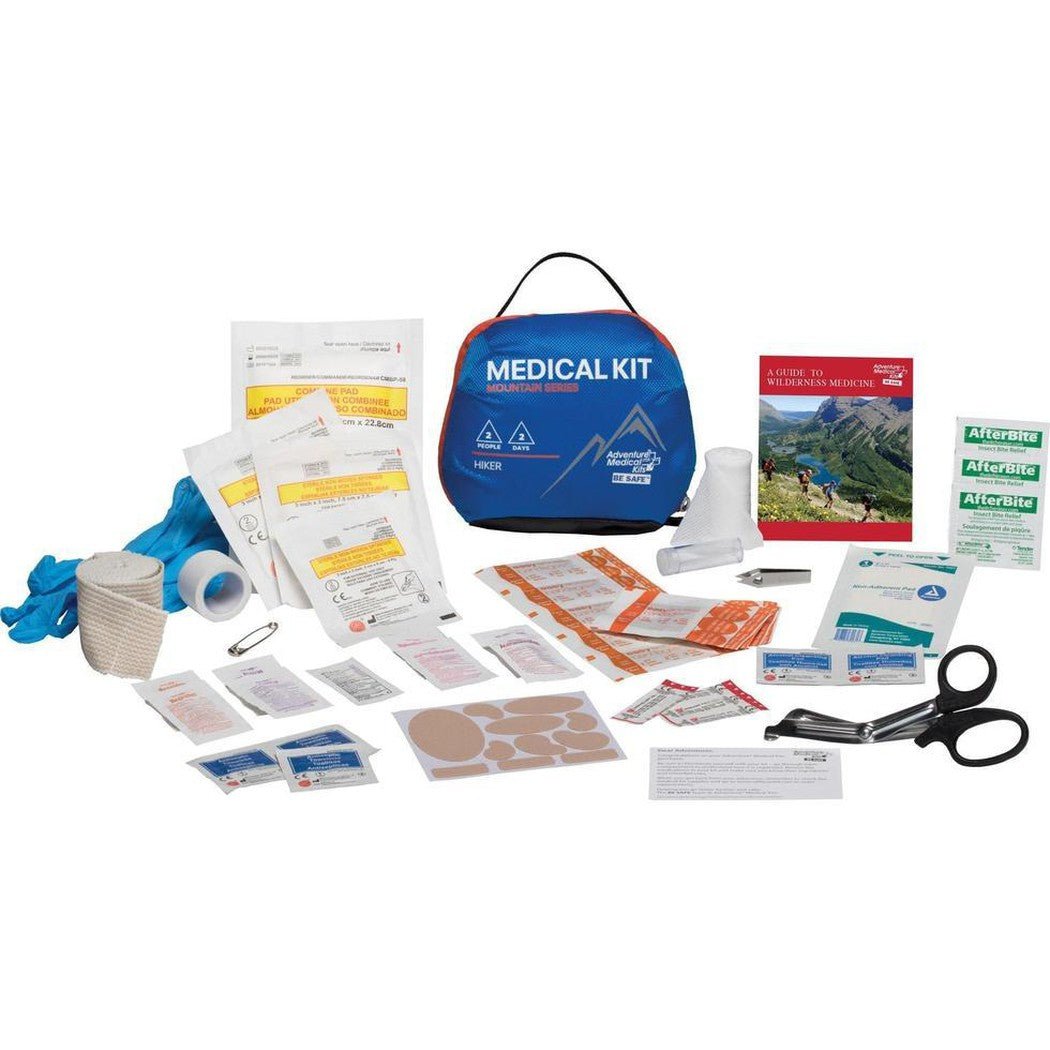 A blue Adventure Medical Kits Mountain Hiker Medical Kit laid out with bandages, scissors, and a first aid guide on a white background.