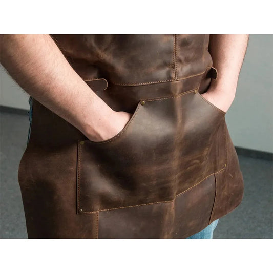 A front view of the Beavercraft Adjustable Brown Leather Work Apron with hands in pockets against a gray background.