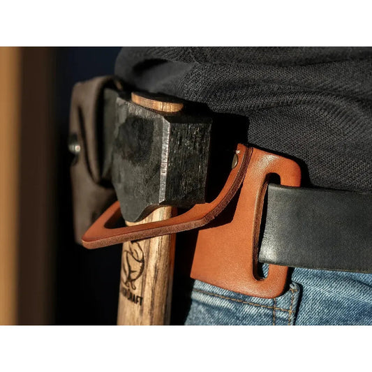 A close-up of a Beavercraft Leather Tool Belt Hanger attached to a black belt, with a wooden axe visible, on a person wearing blue jeans.