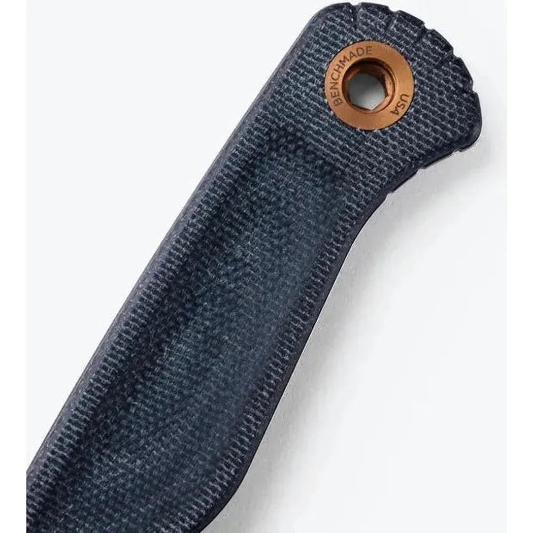 A close-up of the Benchmade Dacian knife handle in charcoal/graphite with a copper lanyard hole and textured grip against a white background.