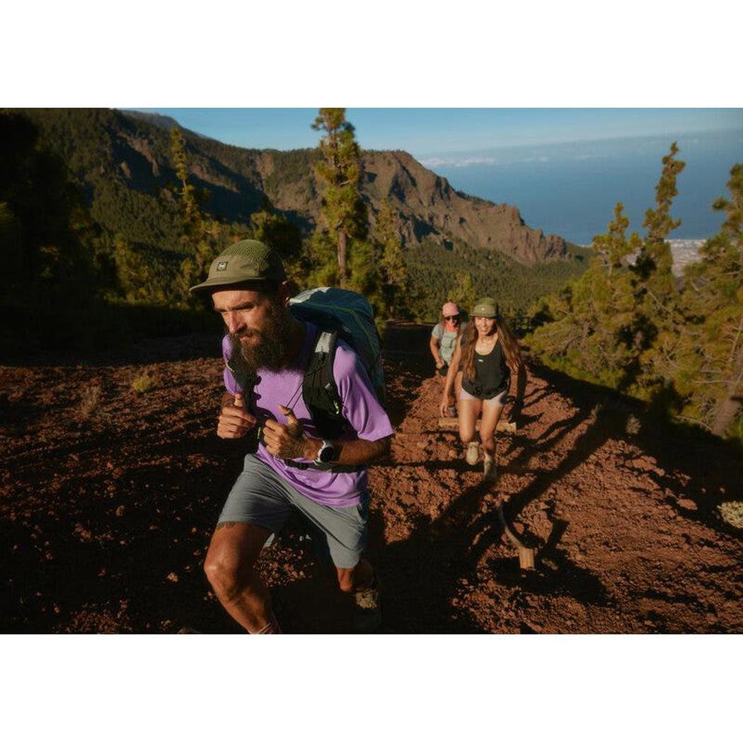 A man hiking in a purple shirt and gray shorts wears the Military Buff 5 Panel Air Cap - Saret as he leads two others up a mountain trail.