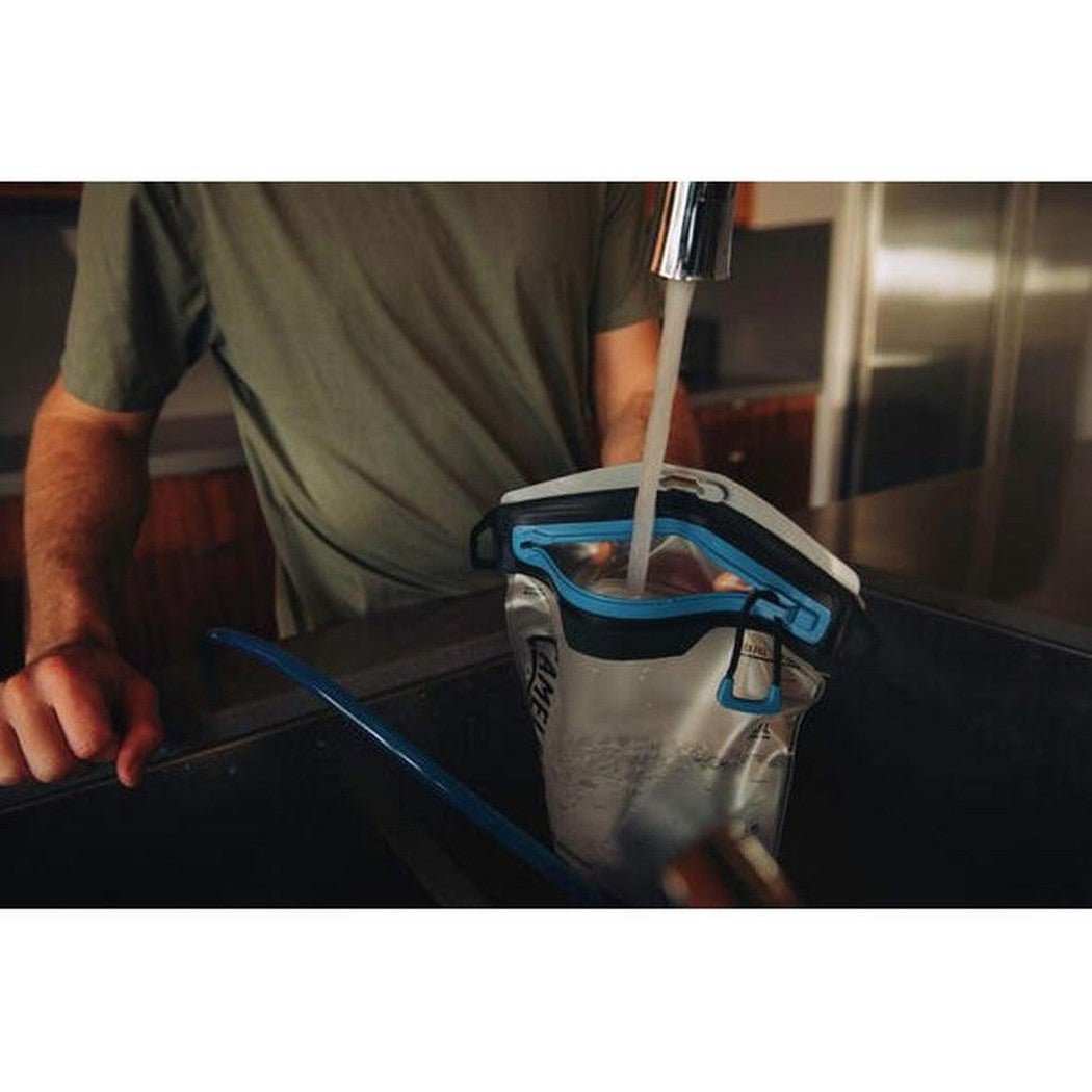 A person fills the CamelBak Fusion Reservoir with water from a faucet in a kitchen setting.