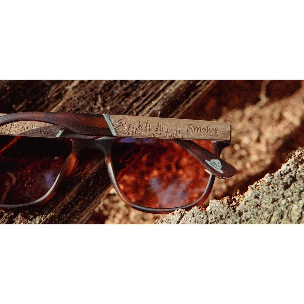 Side view of the Camp Eyewear Trail - Smokey Bear sunglasses with matte tortoise frames and brown lenses resting on a log.