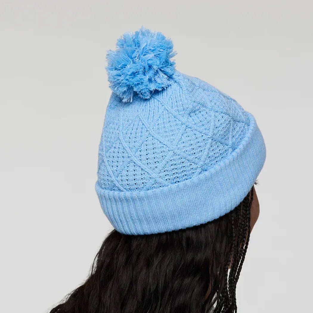 Back view of the Cotopaxi Tozo Beanie in Iceberg with a blue pom pom, on a model with dark hair against a plain background.