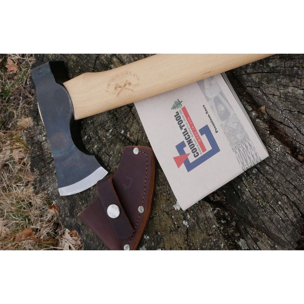 A top-down view of the Council Tool Co. Wood-Craft Camp Carver axe with its leather sheath and instruction manual on a tree stump.