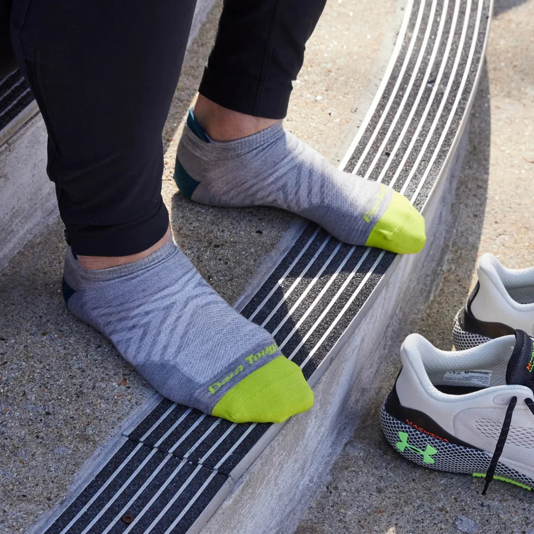 A person wearing gray Darn Tough Men's Run No Show Tab Ultra-Lightweight Running Socks stands on outdoor steps with matching shoes nearby.