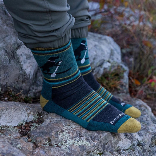 A person wearing Dog Pond Darn Tough Men's Willoughby Micro Crew Lightweight Hiking Socks sits on a rock with a forest background.