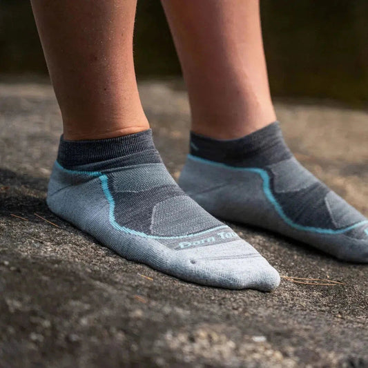 A close-up of a woman’s feet wearing Darn Tough Women's Light Hiker No Show Lightweight with Cushion socks in Slate on a rock surface.