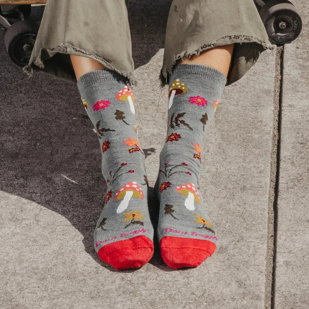 A woman wearing Darn Tough Women's Shroom Bloom Crew Lightweight Lifestyle Socks in Blackberry sits on a skateboard with a concrete background.