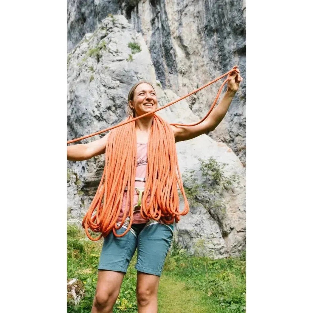 A woman wearing the Edelrid Heron Eco Dry 9.8mm Fire climbing rope stands in front of a rocky cliff face.