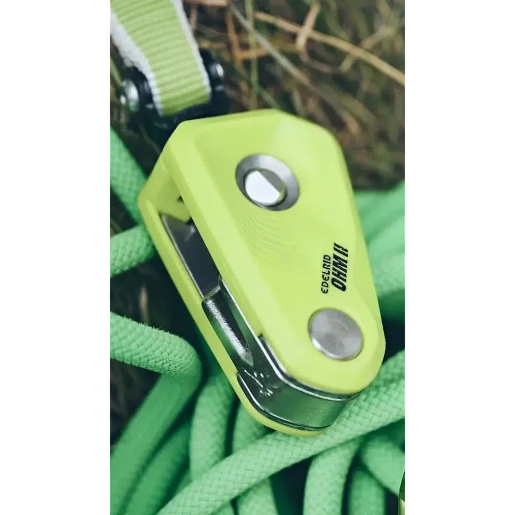 A close-up of the Edelrid Ohm II belay device in Oasis green resting on a green climbing rope with a grassy background.
