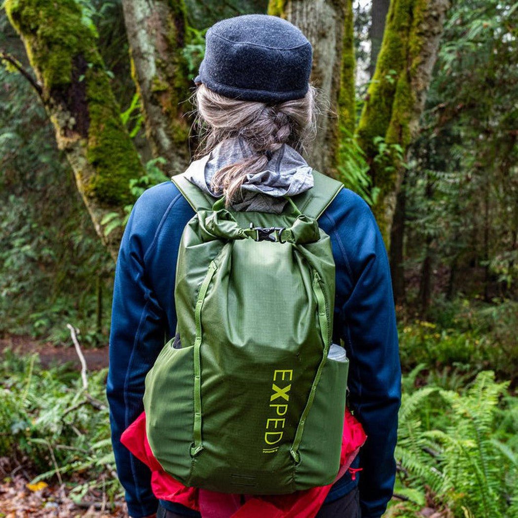 Back view of the black Exped Typhoon daypack on a model in a forest with mossy trees.