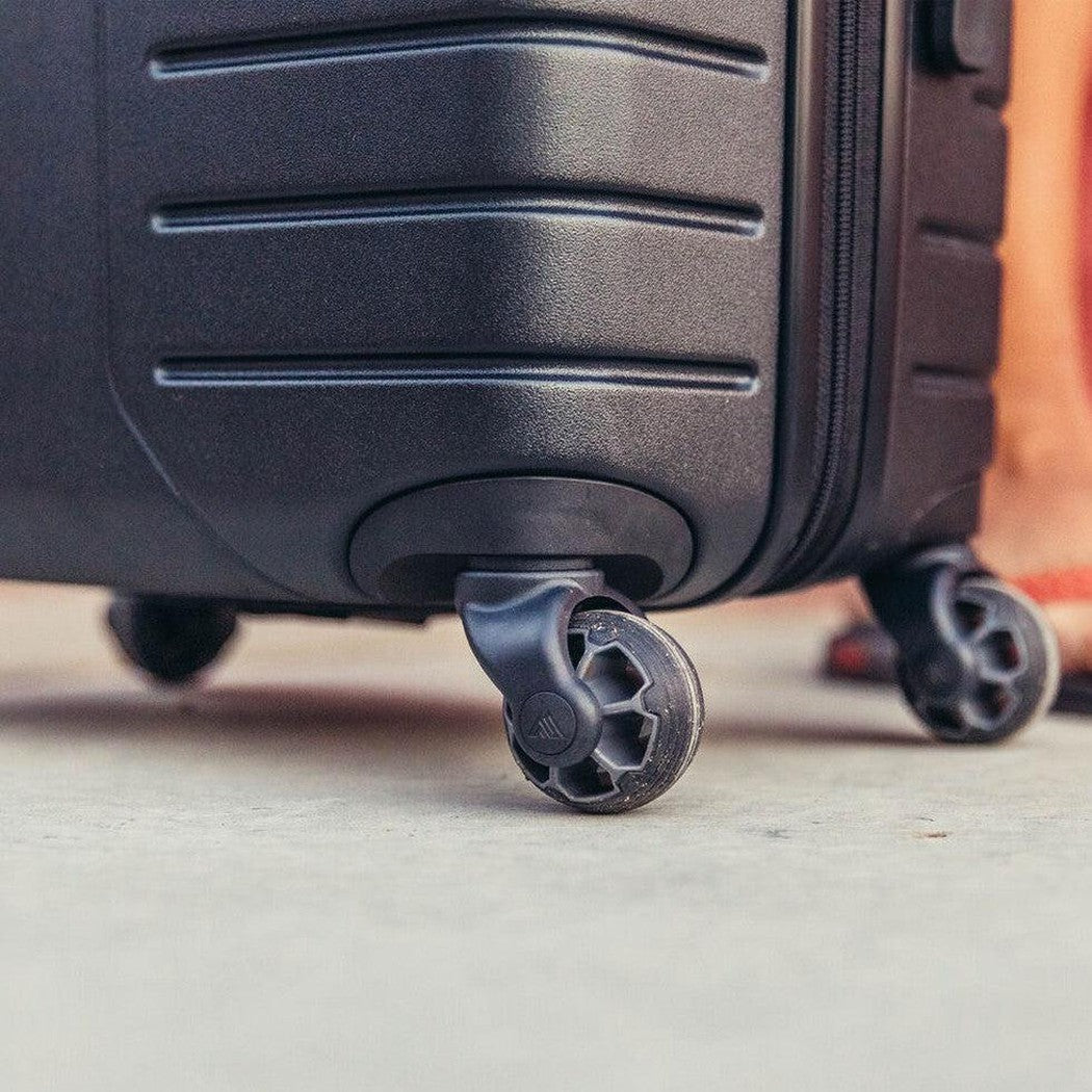 A close-up of the Gregory Quadro Hardcase 22 in Total Black showing the front wheel and zipper against a concrete surface.