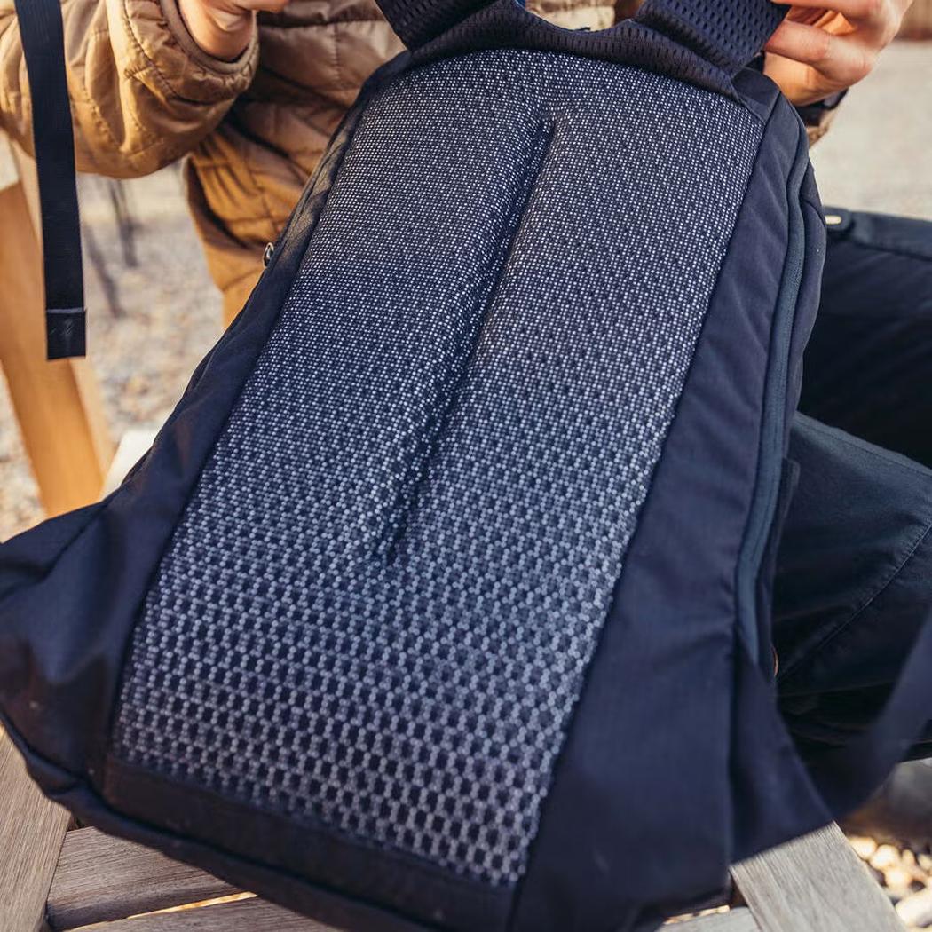 A close-up of the Gregory Rhune 22 daypack in Cabon Black, showing its mesh back panel and a person holding it outdoors.