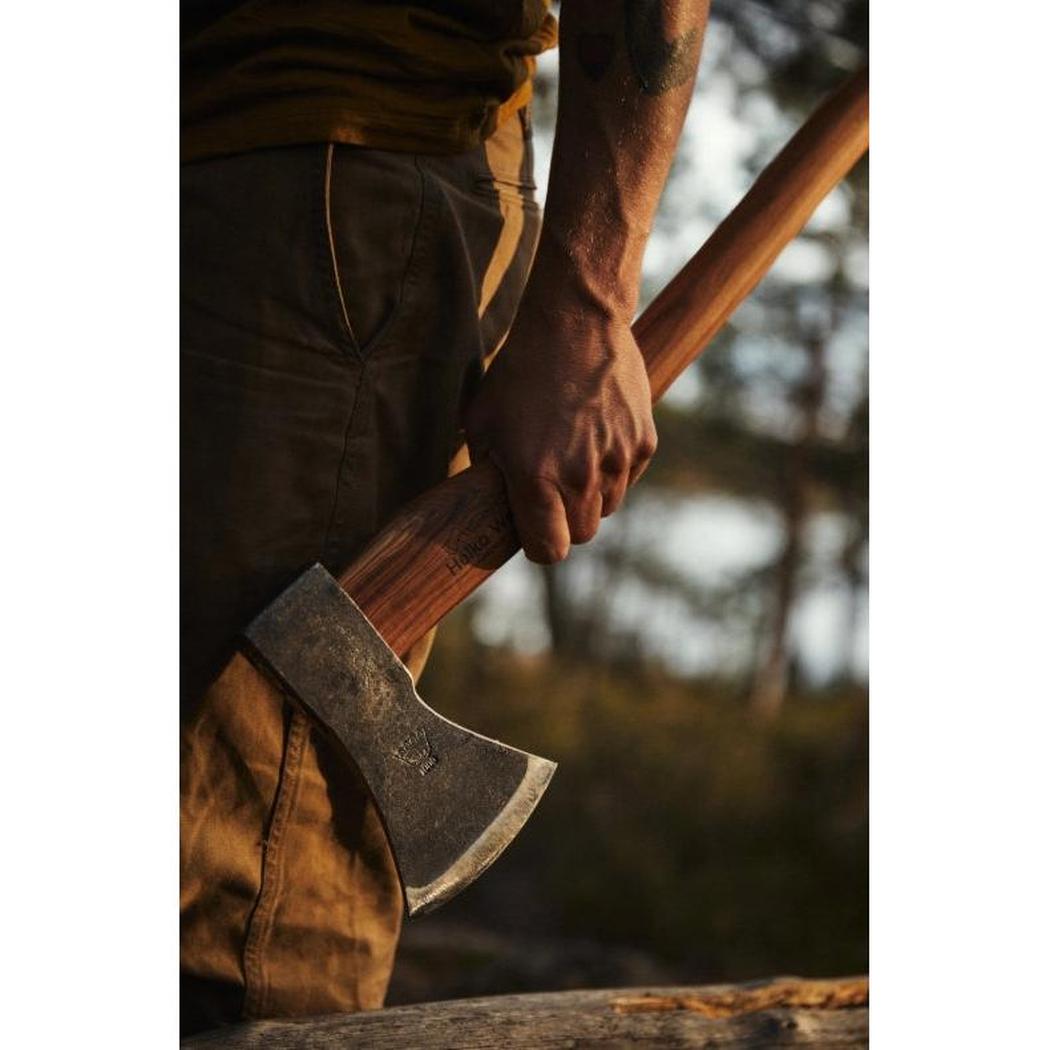 A person holds the Helko Werk Black Forest Woodworker axe with a wooden handle and metal head, against a blurred outdoor background.