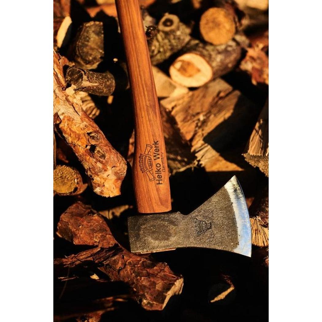 A close-up of the Helko Werk Rheinlander Pack Axe with its wooden handle and metal head resting on a pile of firewood.