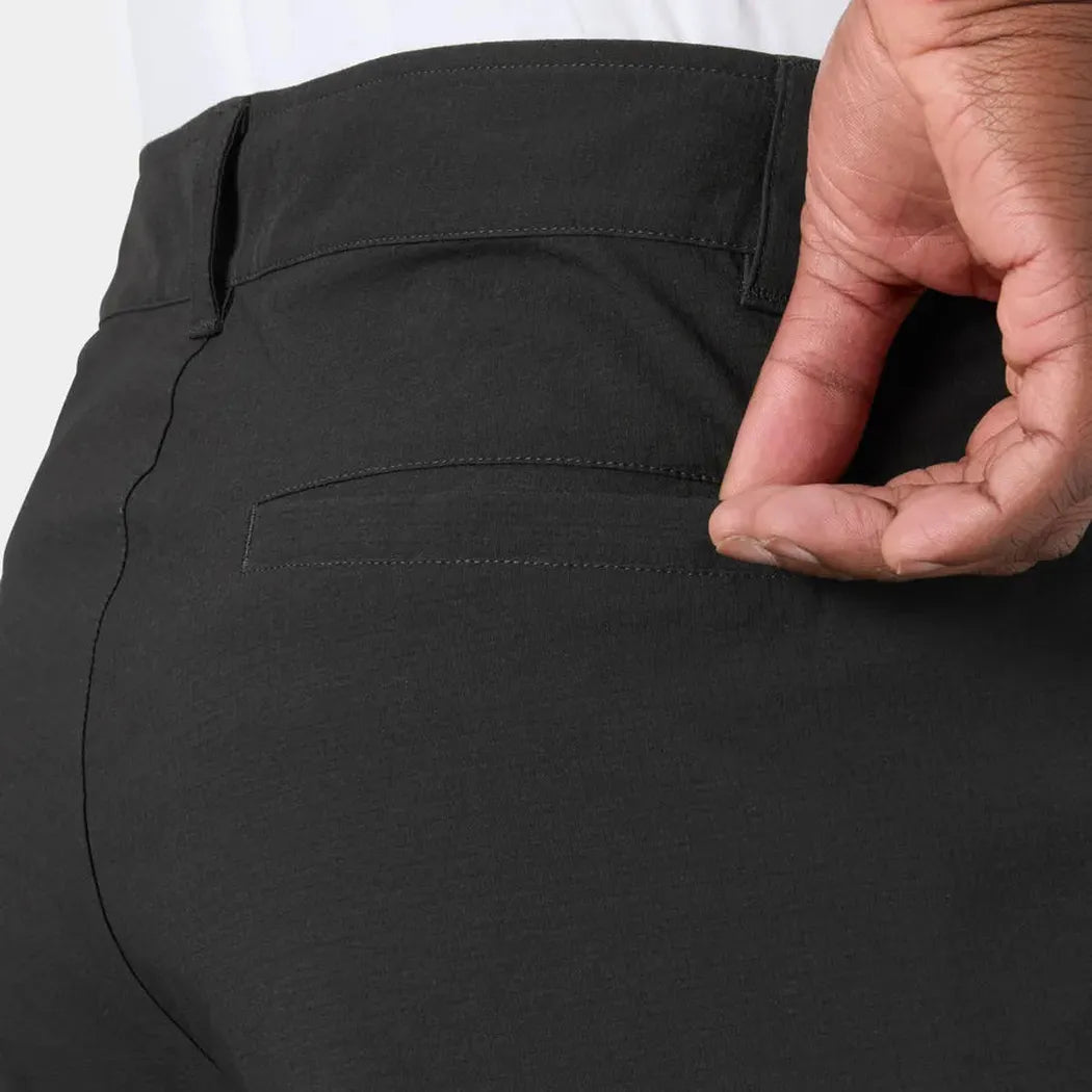 A hand touches the back pocket of the Helly Hansen Men's Move Quick Dry 6” Shorts in Black, showing the fabric and stitching.