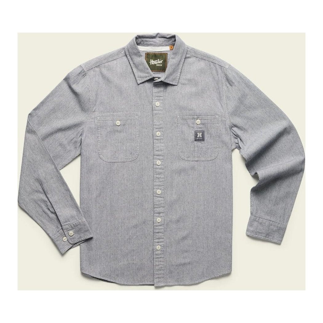A front view of the Howler Brothers Men's Tallier Work Shirt in Hickory Stripe Chambray with two chest pockets and a small logo patch, laid flat against a light background.