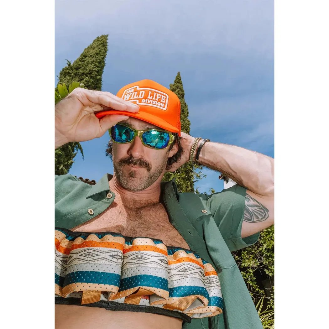 A man wearing a Park Lines Kavu Beer Buddy in front of trees and a blue sky.