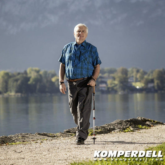 An older man walks by a lake with Komperdell Walker Powerlock trekking poles in a blue shirt.
