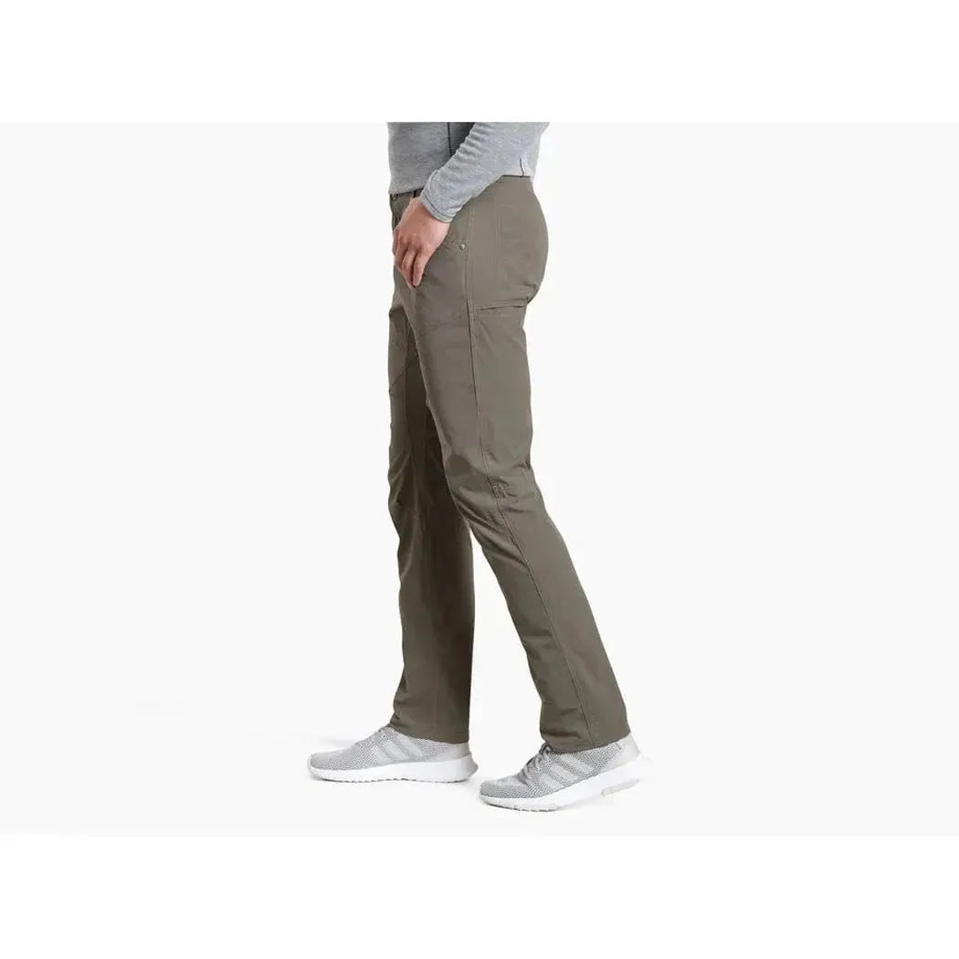 Side view of the Kuhl Men's Silencr Pant in Storm Khaki on a model wearing light gray sneakers against a white background.