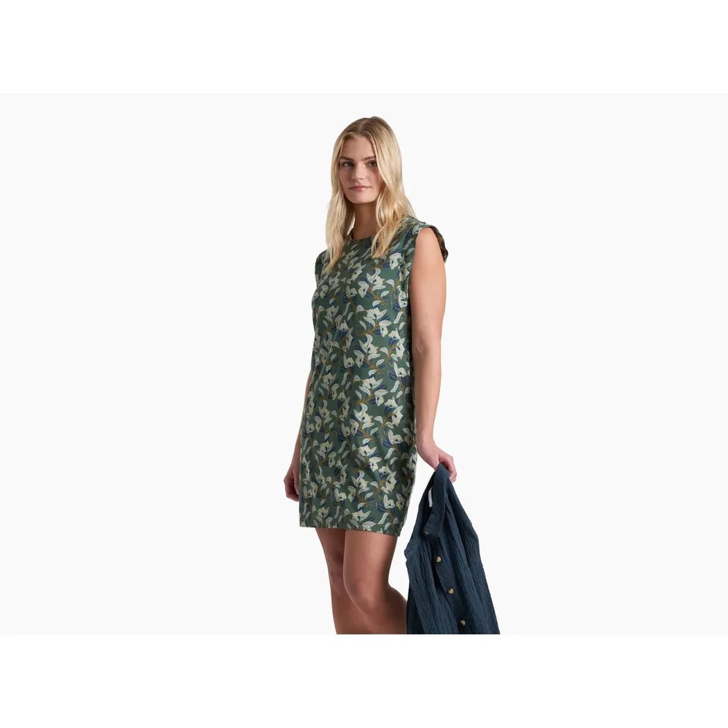 A model wears the Kuhl Women's Lyra Tee Dress in Smoked Pine Print, holding a jacket, against a plain white background.