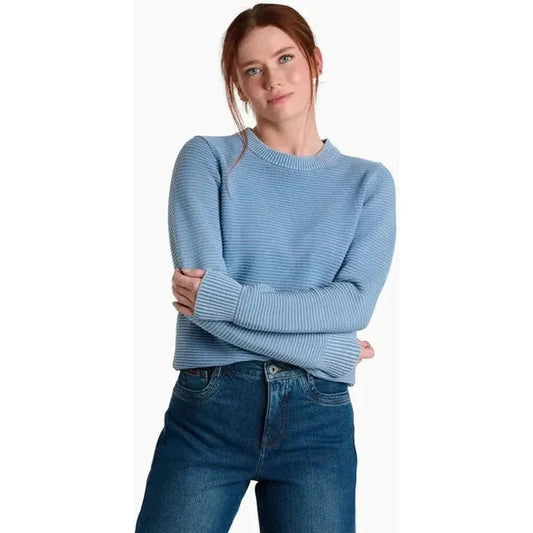 A model wearing the Kuhl Women's Sofie Sweater in Metal Blue stands against a white background with her arms crossed.