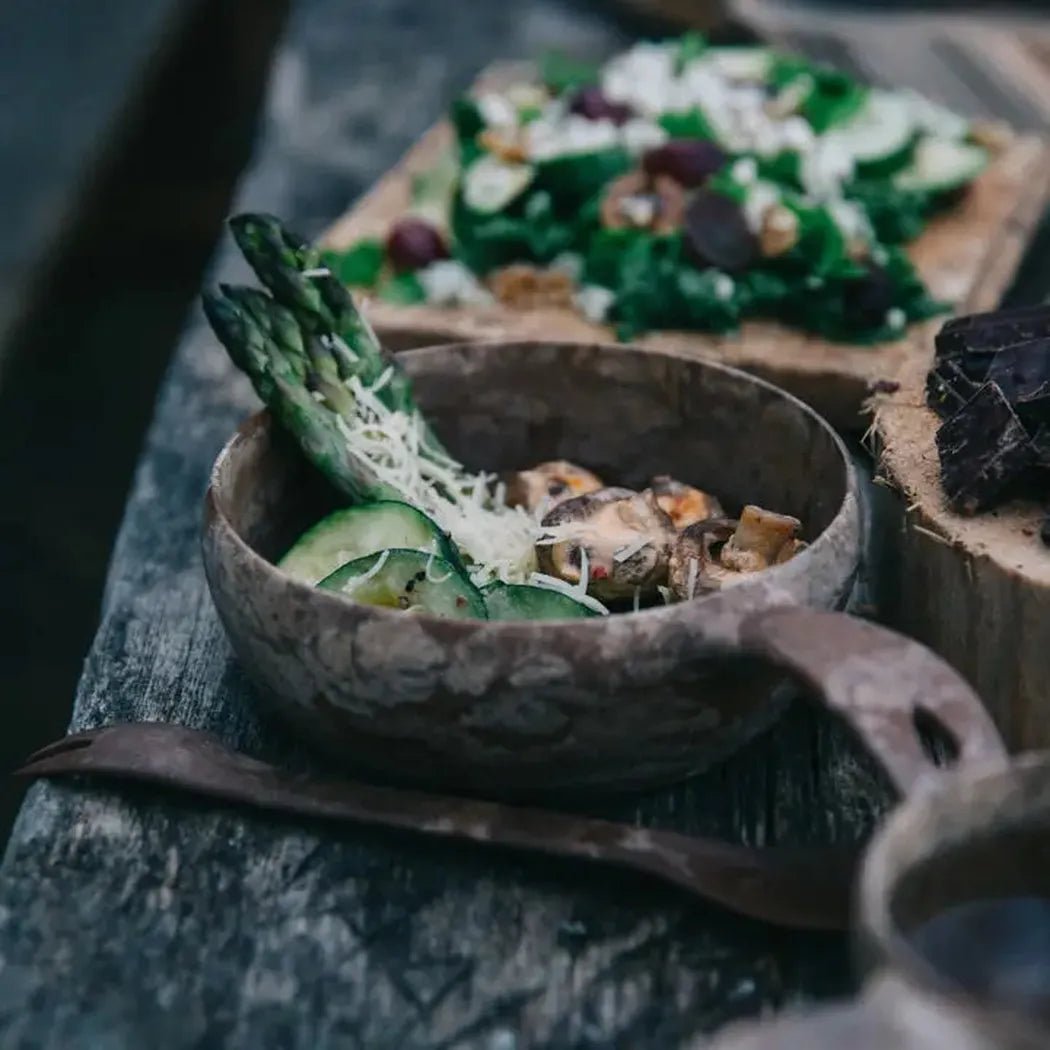 A close-up of the Kupilka 55 Soup Bowl in Black on a weathered wooden table with a salad in the background.