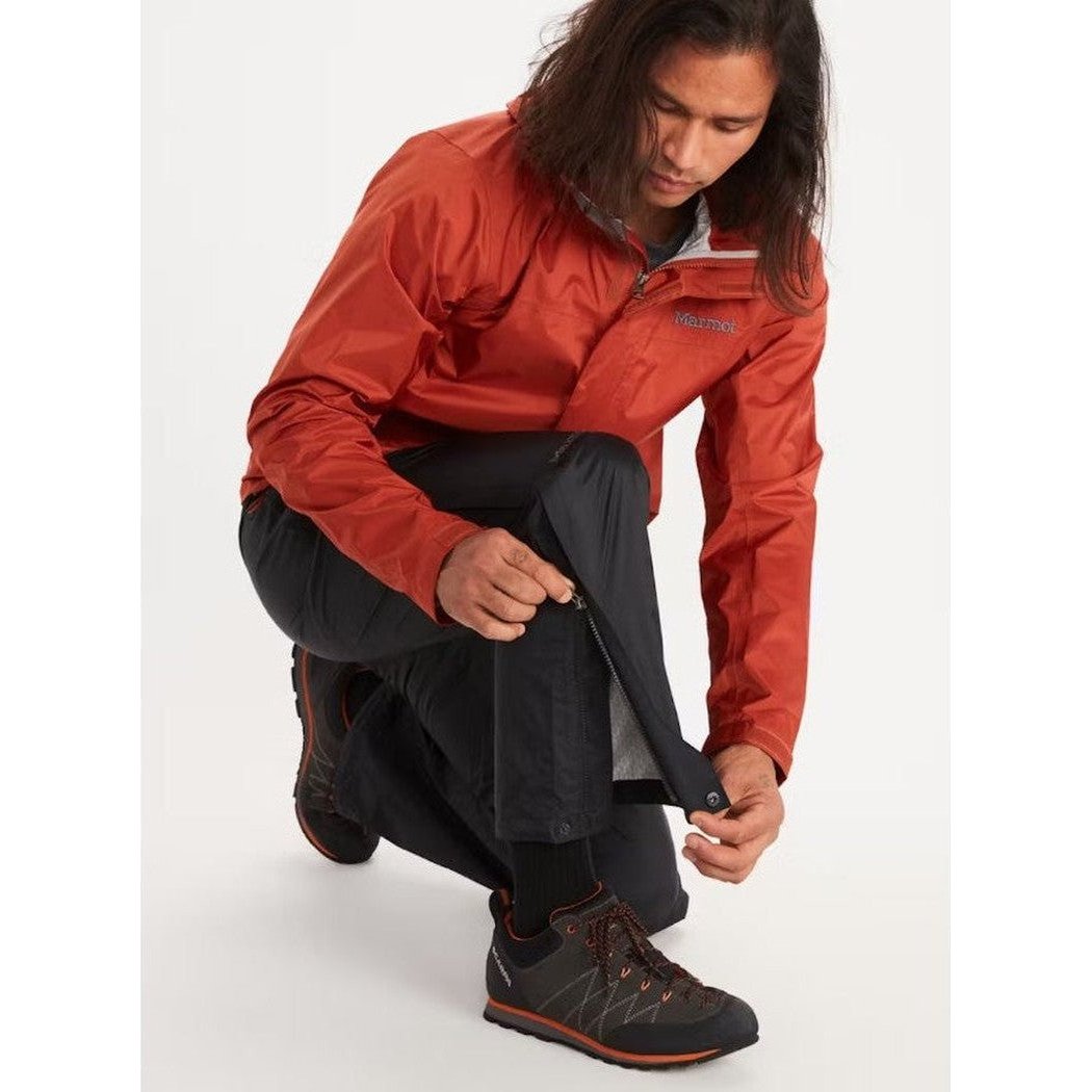 A model wearing the Marmot Men's PreCip Eco Full Zip Pant in Black adjusts the leg while kneeling on a white background.