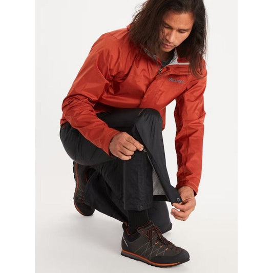 A model wearing the Marmot Men's PreCip Eco Full Zip Pant in Black adjusts the leg while kneeling on a white background.
