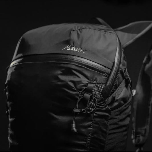 A close-up of the Matador Freefly 16 Packable Backpack in Black, showing the front zipper and logo against a dark background.