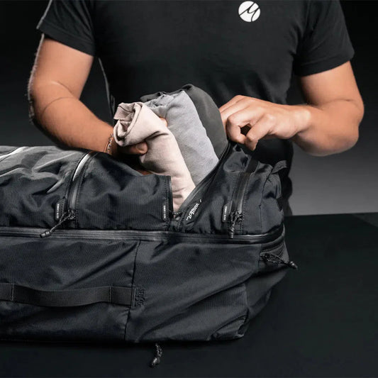 A person packing a black Matador SEG 45 Travel Pack with clothing on a dark surface.