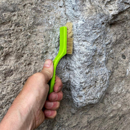 A hand holds the Metolius Razorback Boar's Hair Brush against a gray rock face.