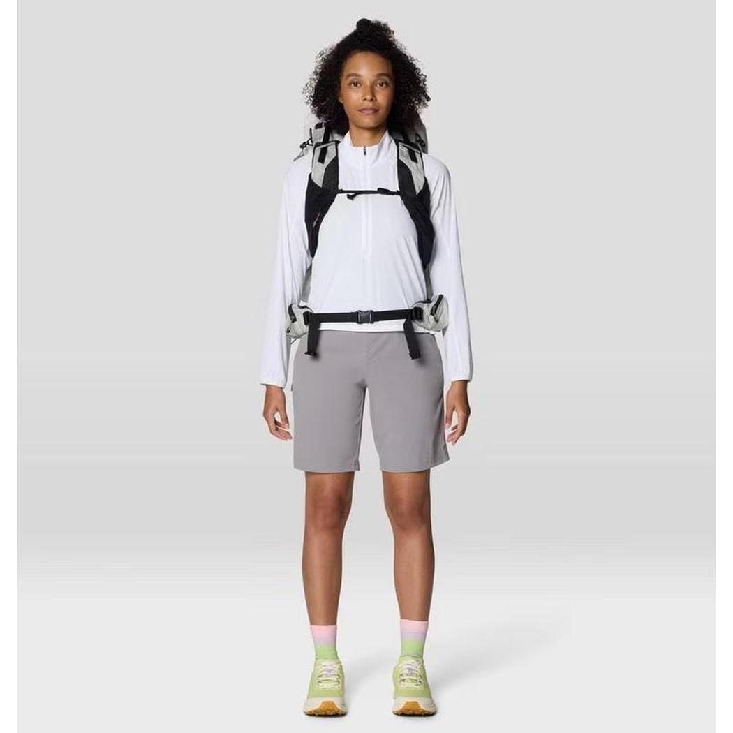 A front view of the Mountain Hardwear Women's Sunshield Half Zip in Fogbank on a model with a backpack and gray shorts against a plain background.