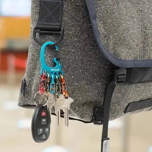 A close-up of the Nite Ize BigFoot Locker KeyRack Aluminum in Assorted colors attached to a charcoal/gray bag strap, showing keys and a car remote.