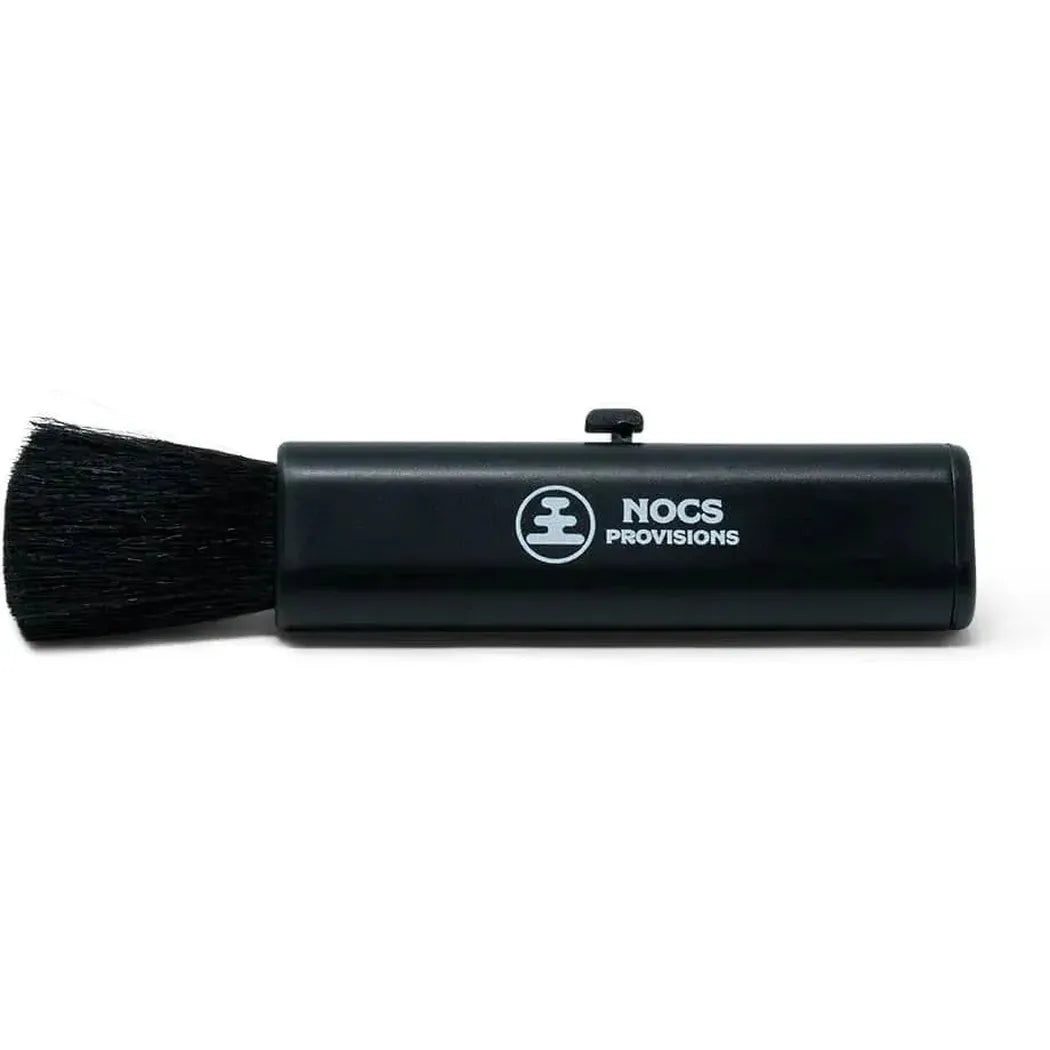 A black Nocs Provisions cleaning kit with a brush head and a small button on top, photographed from a front angle against a white background.