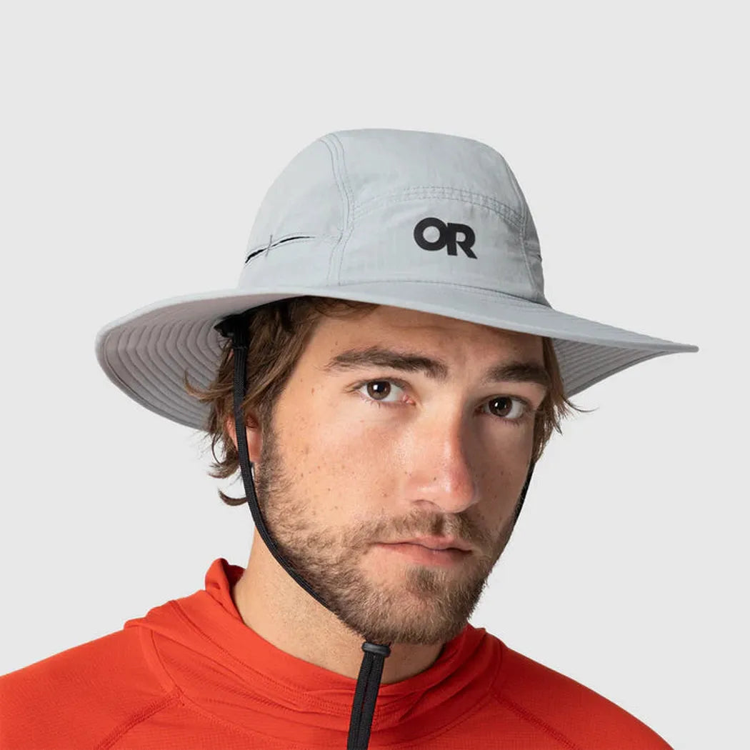 A front view of the Outdoor Research Sunbriolet Sun Hat in Gravel on a model wearing an orange top against a plain background.