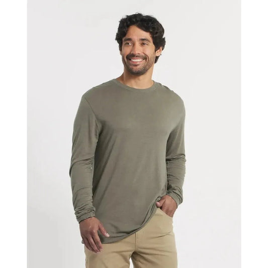 A man wearing the Paka Apparel Mens Aire Long Sleeve in Andean Moss stands against a plain white background.