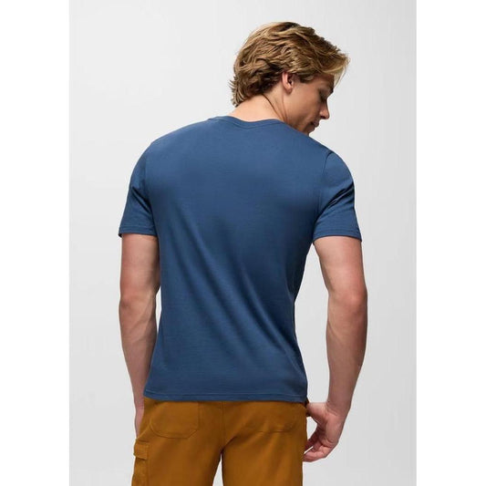 Back view of the Prana Men's Bear Squeeze Journeyman SS Tee in Bluff Blue on a model wearing brown pants against a plain background.