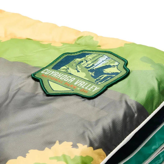 A close-up of the Rumpl Cuyahoga Valley National Park Original Puffy blanket showing the patch and colorful pattern against a white background.