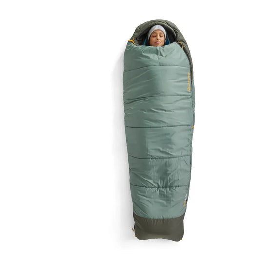 A person wearing a gray beanie is inside the Sea To Summit Boab Synthetic Sleeping Bag 30F|-1C, which is Laurel Wreath Green with a dark gray bottom, shown from a top-down angle against a white