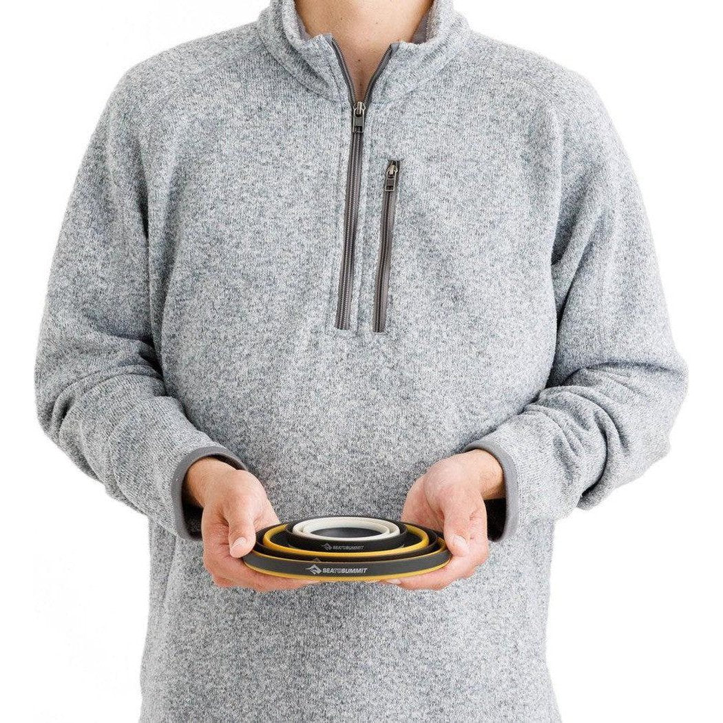 A person in a gray fleece holds the Sea To Summit Frontier UL Collapsible Dinnerware Set Multi against a white background.