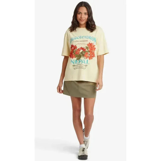 A woman wearing the Sherpa Adventure Gear Women's Tarcho Rhodoendron Tee in Butter stands against a white background.
