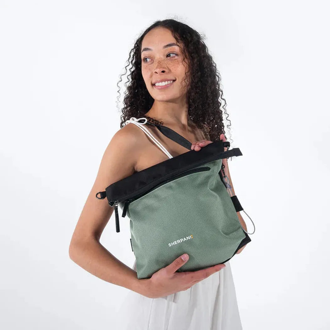 A woman holds the Sherpani Vale AT bag in Aloe Mist against a white background.