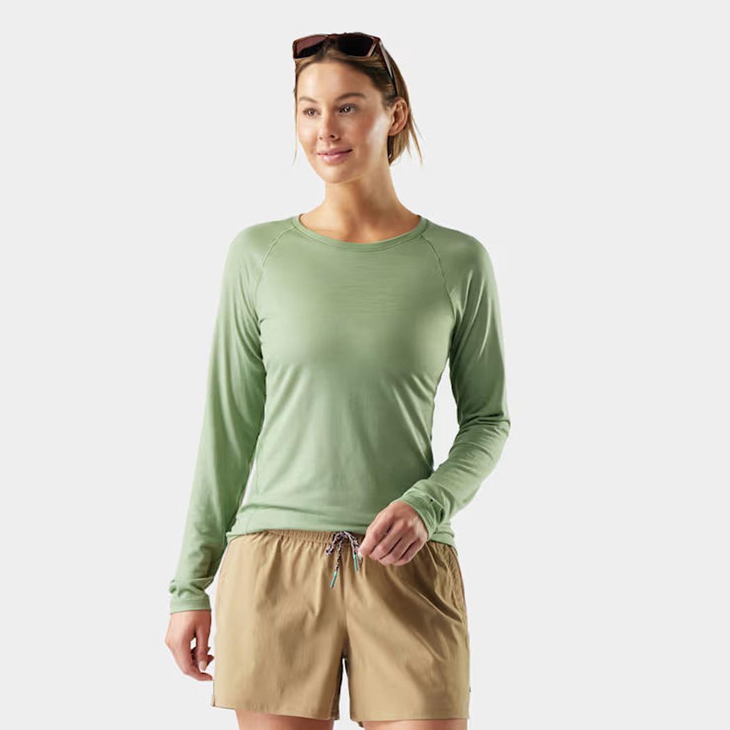 A woman wearing the Smartwool Women's Classic All-Season Merino Base Layer Crew in Green Tea stands against a plain white background.