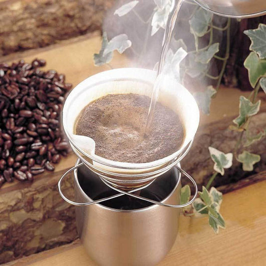 A Soto Outdoors Helix Coffee Maker brewing coffee with steam rising, placed on a wooden surface near coffee beans and ivy.
