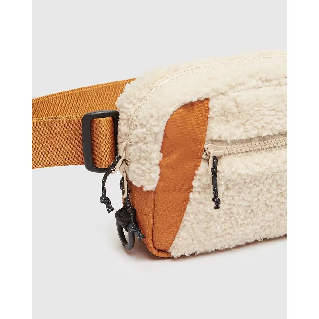 A close-up of the Tentree Valdes Hip Pack in BurCarameWarOak with a brown strap and zipper pocket, photographed against a plain white background.