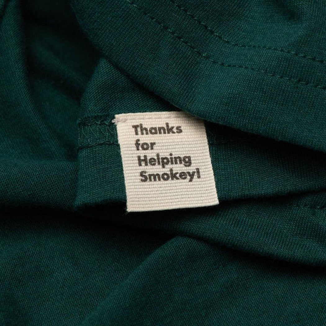 A close-up of the Spruce + Golden The Landmark Project Smokey's Friends Ringer Tee showing the tag and dark green fabric.